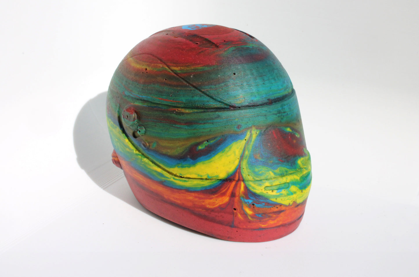 Front side top angle of Custom-made concrete mini Formula 1 helmet designed with vibrant red, blue, and yellow colors, resembling a galaxy theme. The helmet, crafted from concrete/Jesmonite, showcases intricate details and a glossy finish, reflecting the cosmos. Available for purchase with customization options on the website.